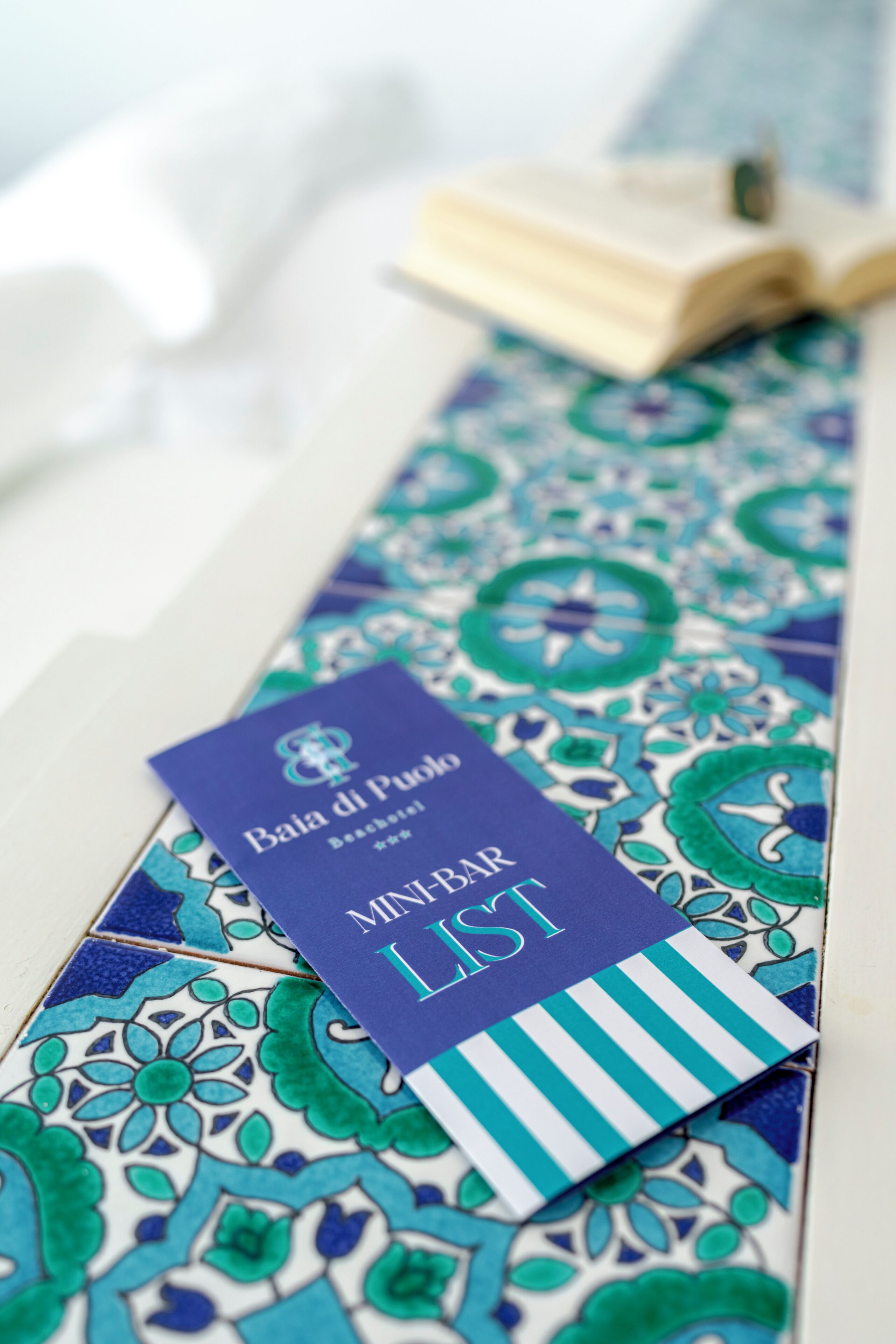 Een blauw-wit geruit das met een label waarop staat 'Baia di Puolo Beach Hotel' en 'MINIBAR LIST'.