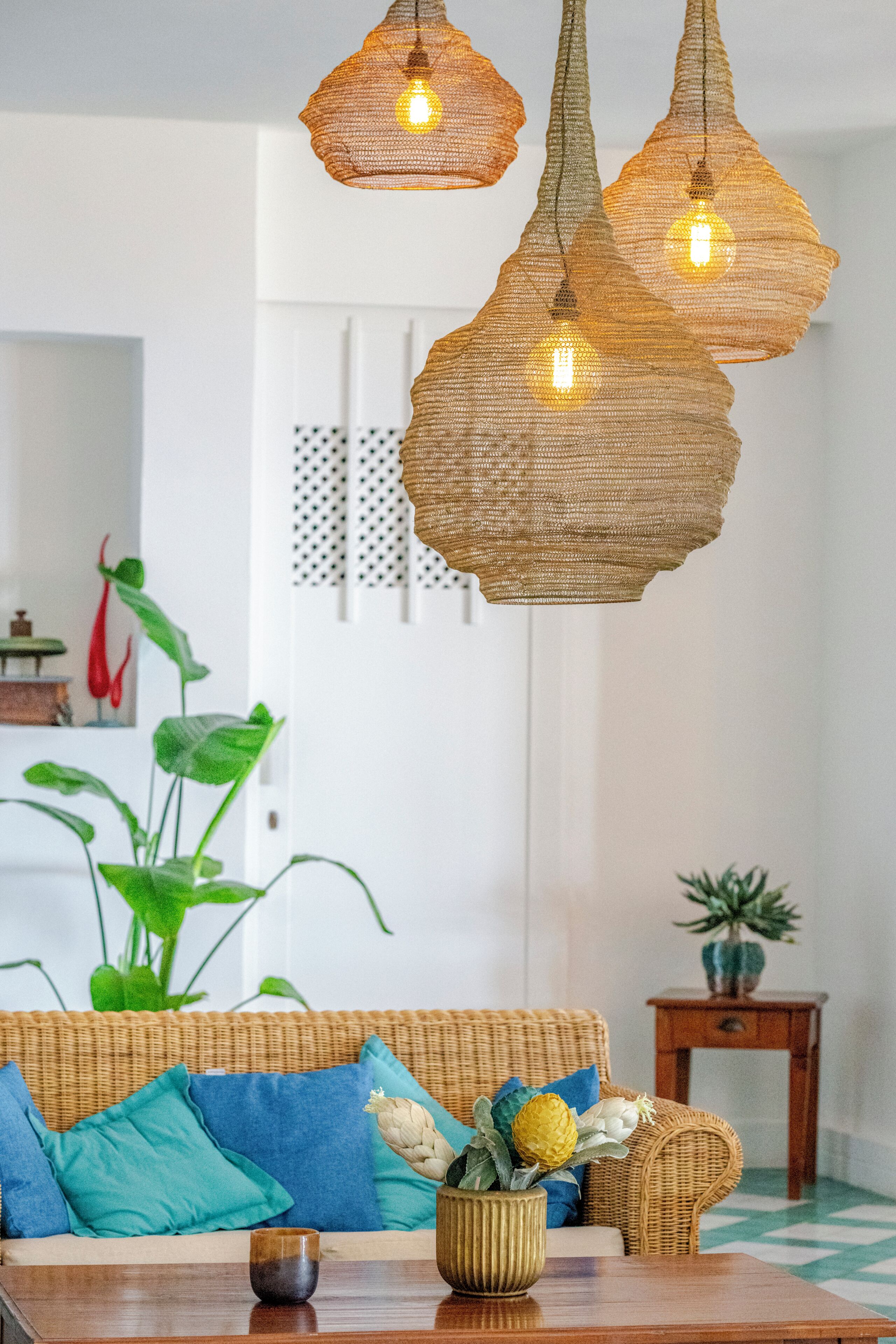 Une pièce avec un canapé en osier, une petite table en bois et des lampes en osier suspendues au plafond.
