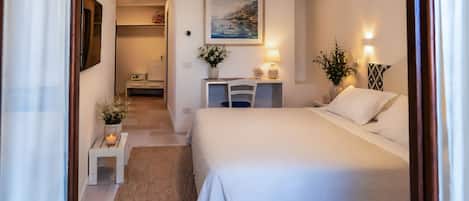 A hotel room with a bed, bedside table, lamp, and a painting on the wall.