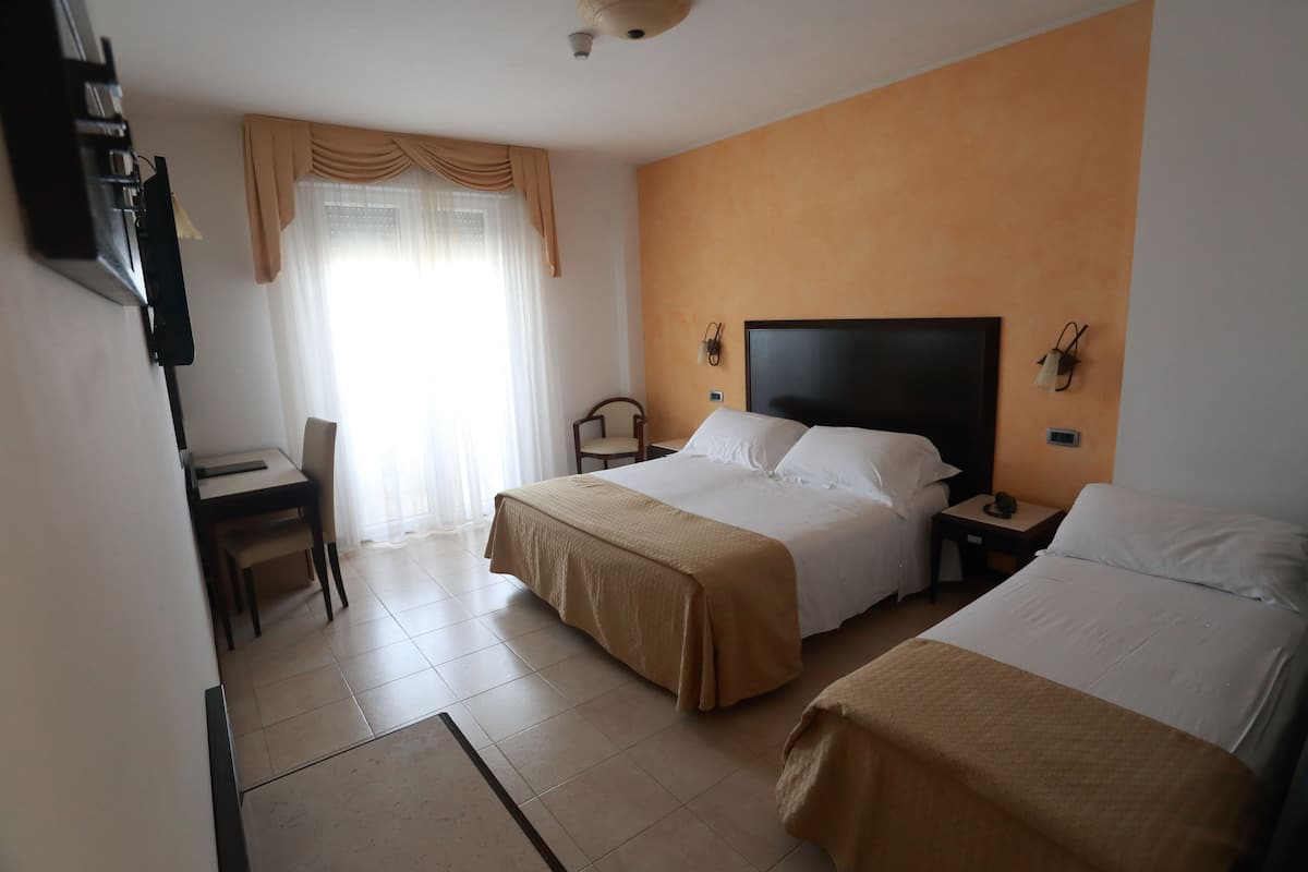 A hotel room with two beds, a desk, a chair, and a television.