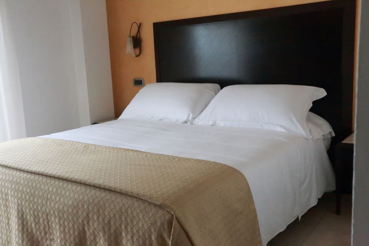 A neatly made bed with white linens and a beige quilted blanket.