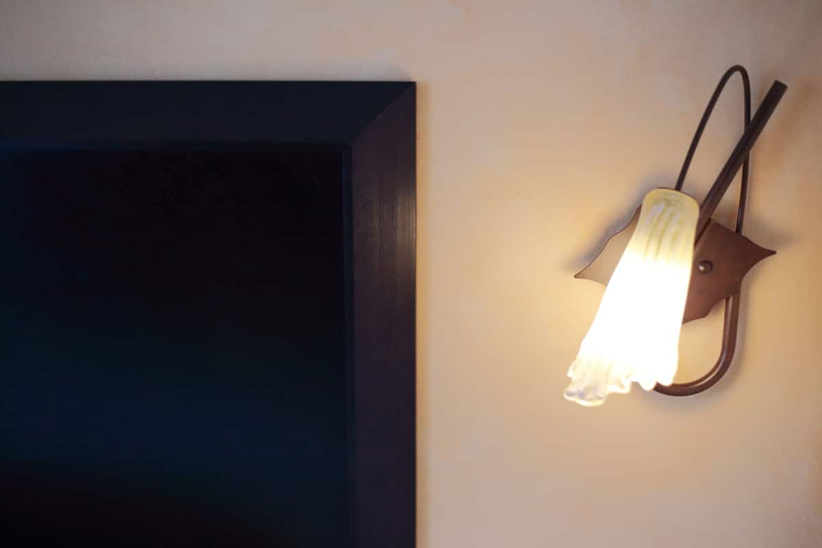 A wall-mounted light fixture with a unique design, possibly a wall sconce, against a plain wall.