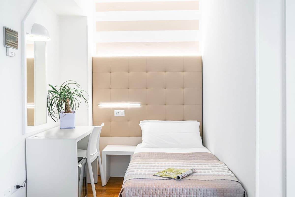 Un dormitorio con cama, mesita de noche, silla y una planta en maceta.