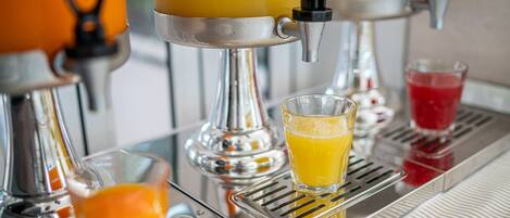 A juice dispenser with a glass of orange juice and a glass of red juice.