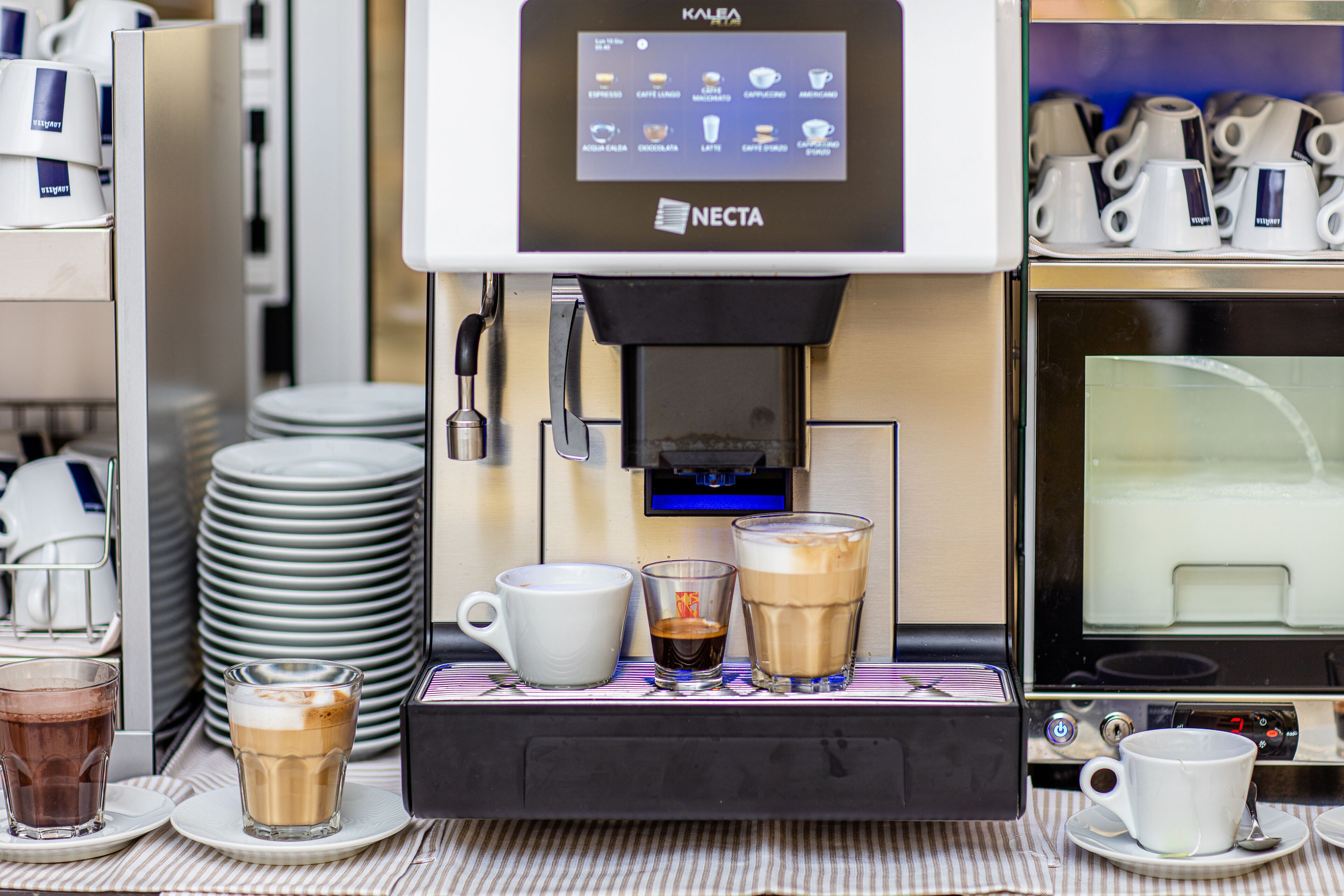 A coffee machine with a digital display, dispensing coffee into cups and glasses.