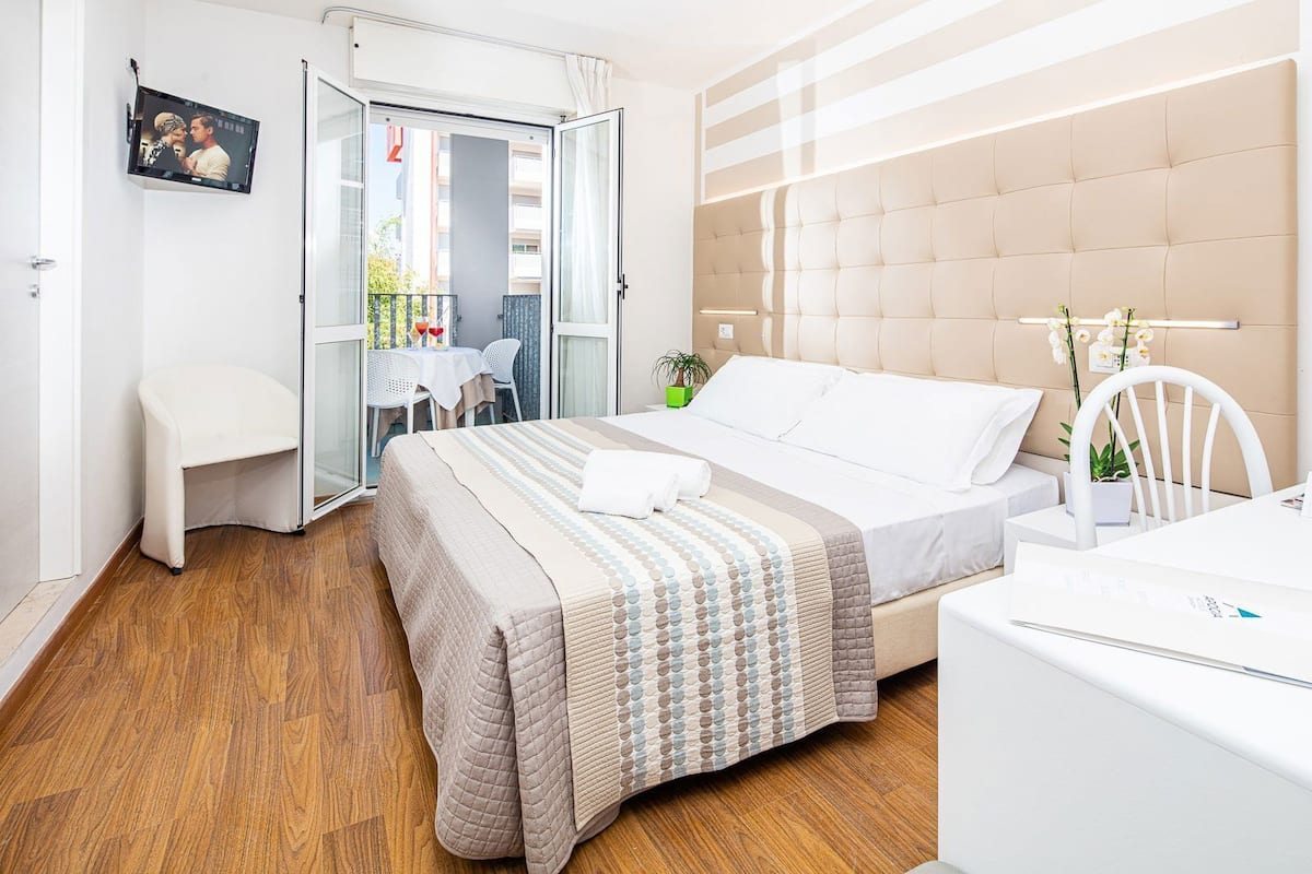 Una habitación de hotel moderna con una cama grande, un escritorio, una silla y un balcón con mesa y sillas.