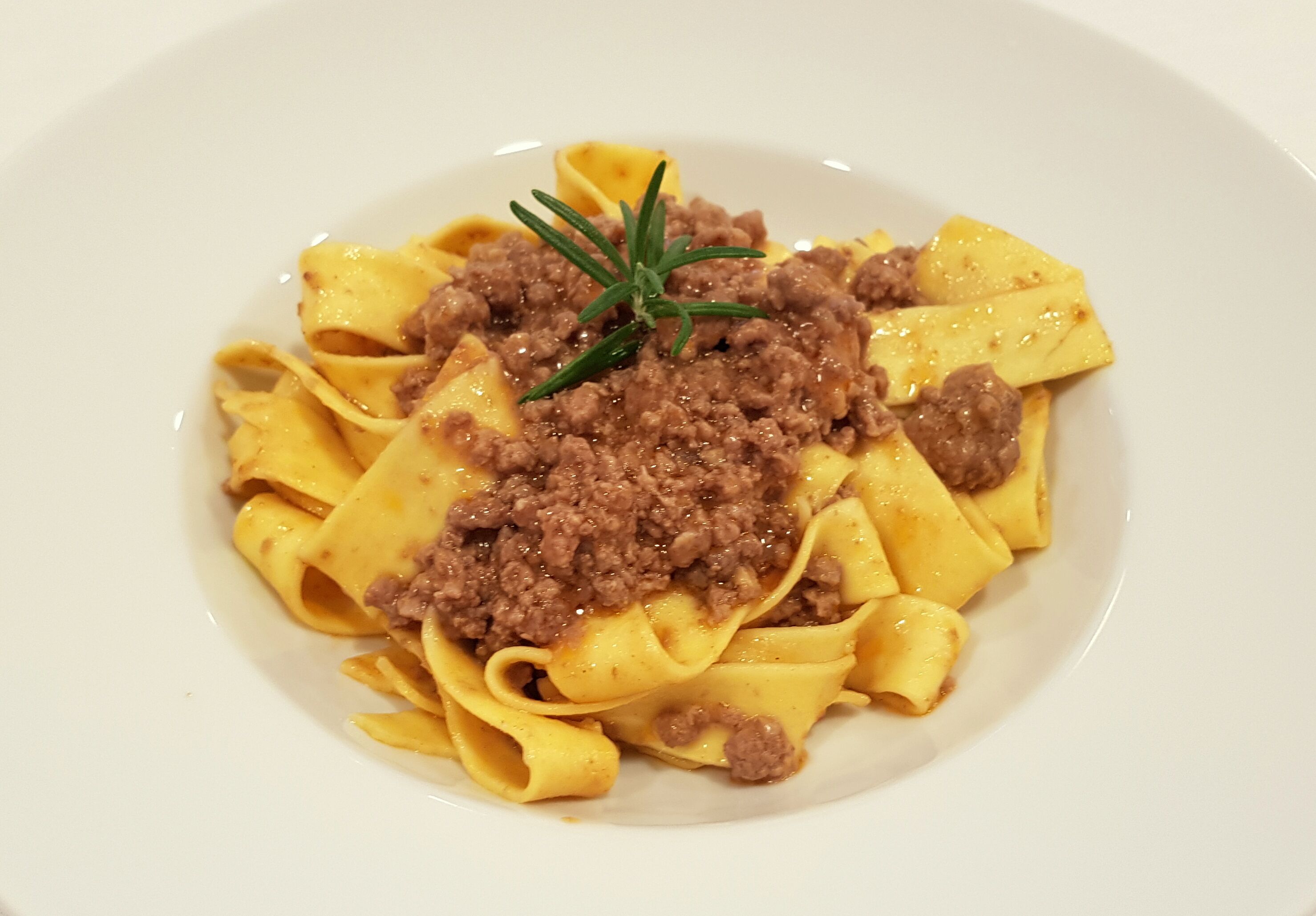 En tallerken med fettuccine pasta, kødsovs og en kvist rosmarin.
