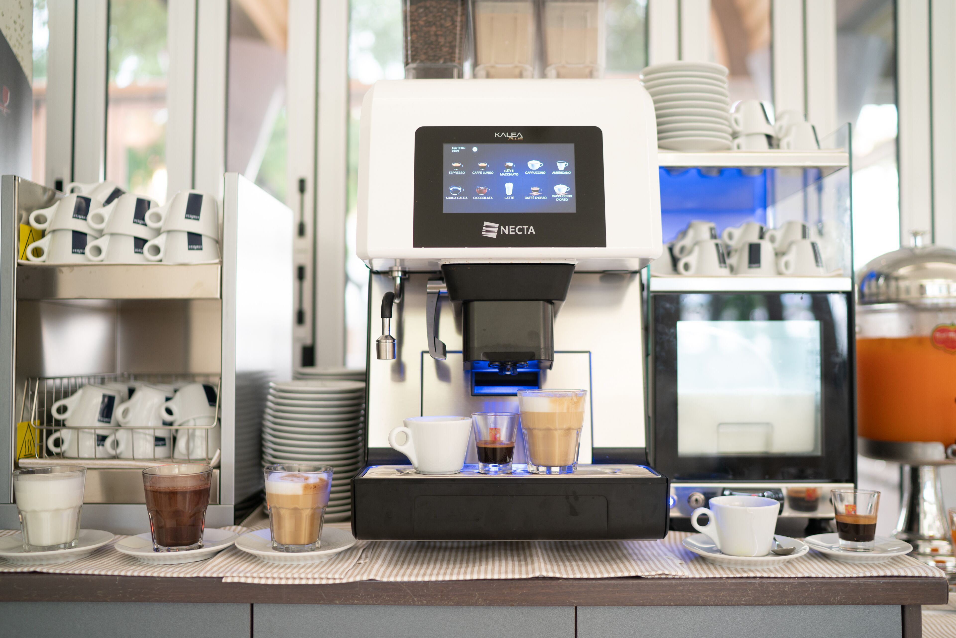 A coffee machine with multiple drink options, cups, and saucers on a counter.