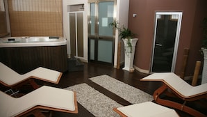 Een wellnessruimte met een jacuzzi, twee lounge fauteuils, een plant en een schuifdeur.