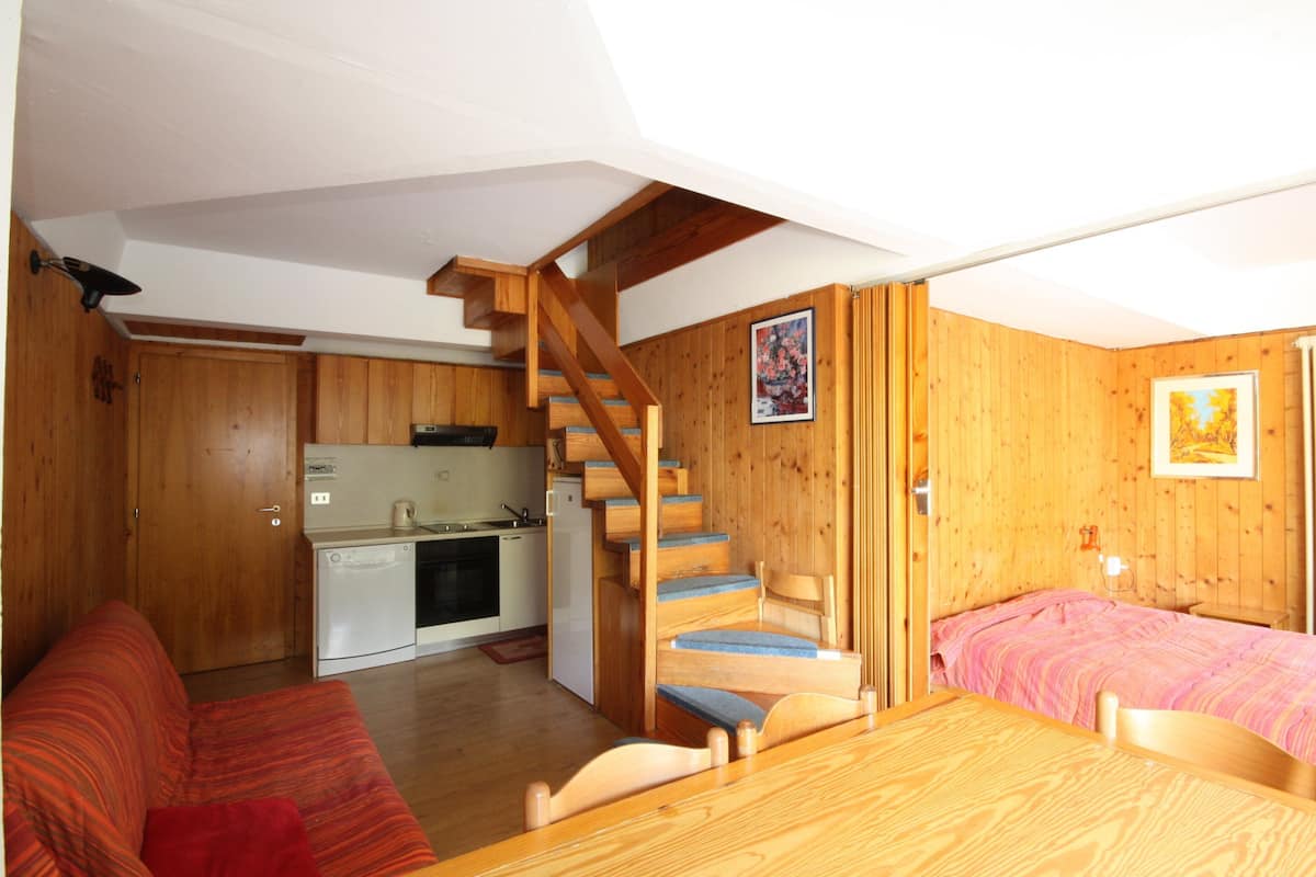 A compact room with a wooden staircase, a kitchenette, a bed, and a sofa.