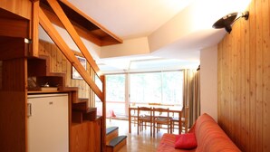 A compact room with a wooden staircase, a small kitchenette, a sofa, and a dining area with chairs and a table. - Residence Sole Alto (Mezzana)