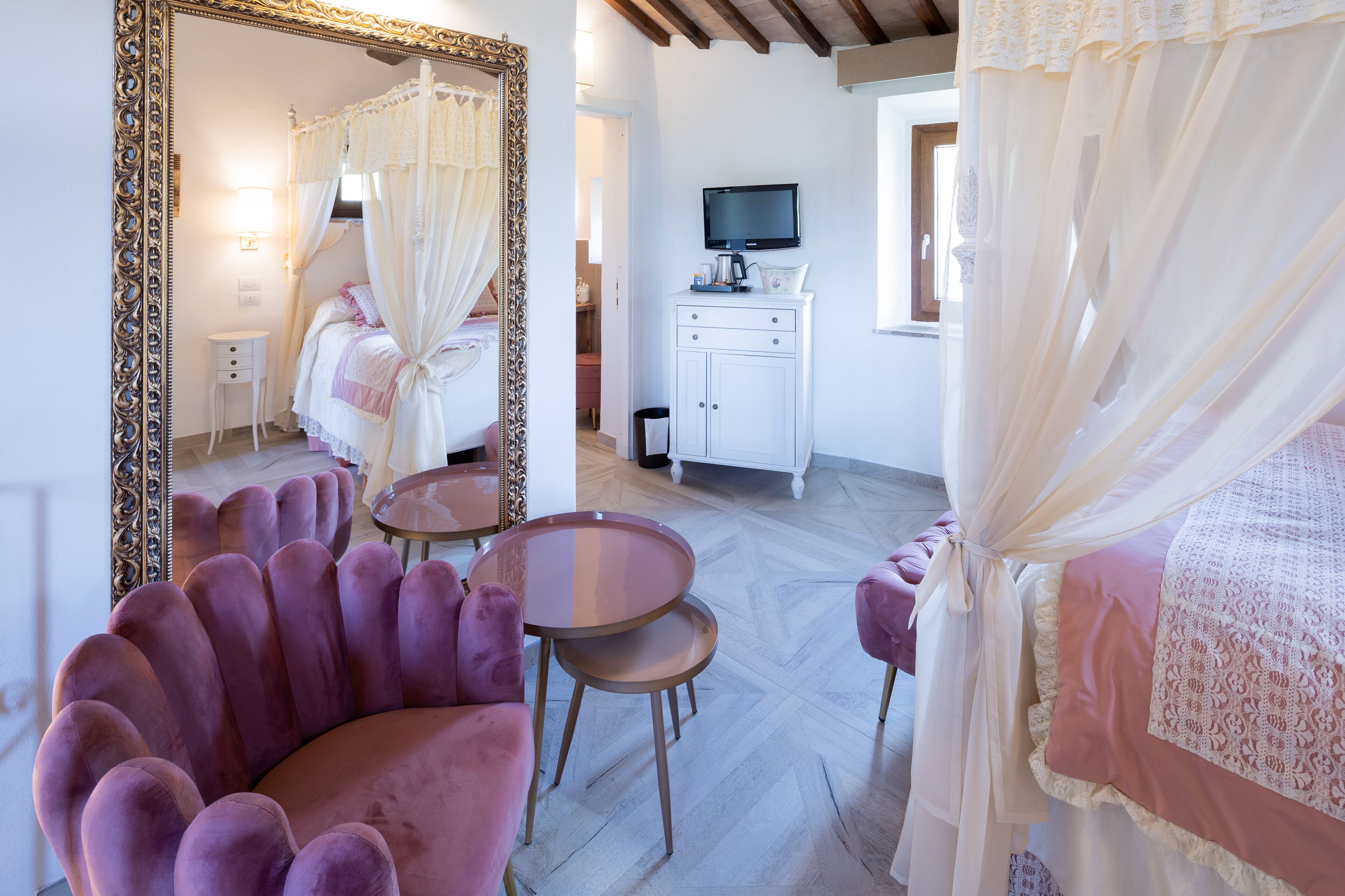 A bedroom with a bed, a vanity with a mirror, a television, and a small table.