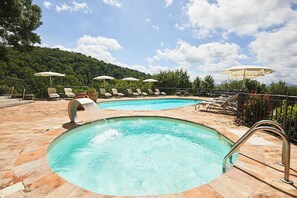 A swimming pool with a waterfall feature, surrounded by lounge chairs and umbrellas. - Il Castelluccio Country Resort (Barberino di Mugello)