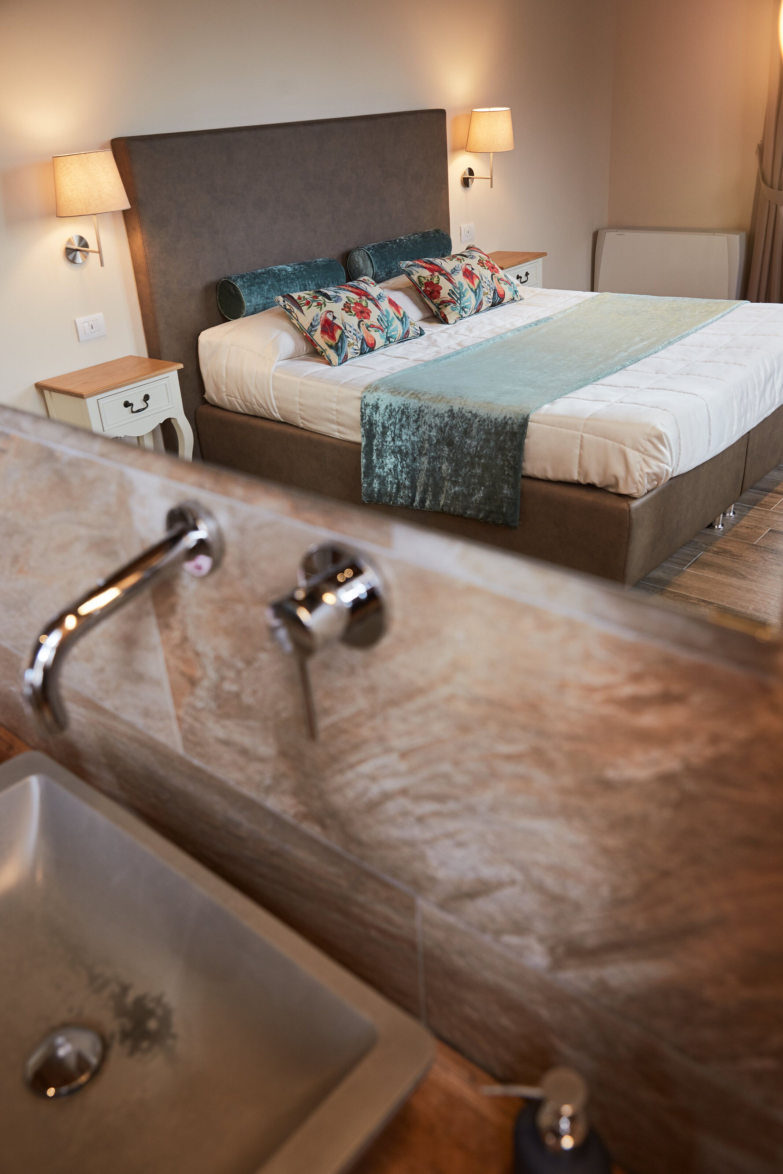 A hotel room with a bed, two bedside lamps, a nightstand, and a bathroom with a sink and shower.