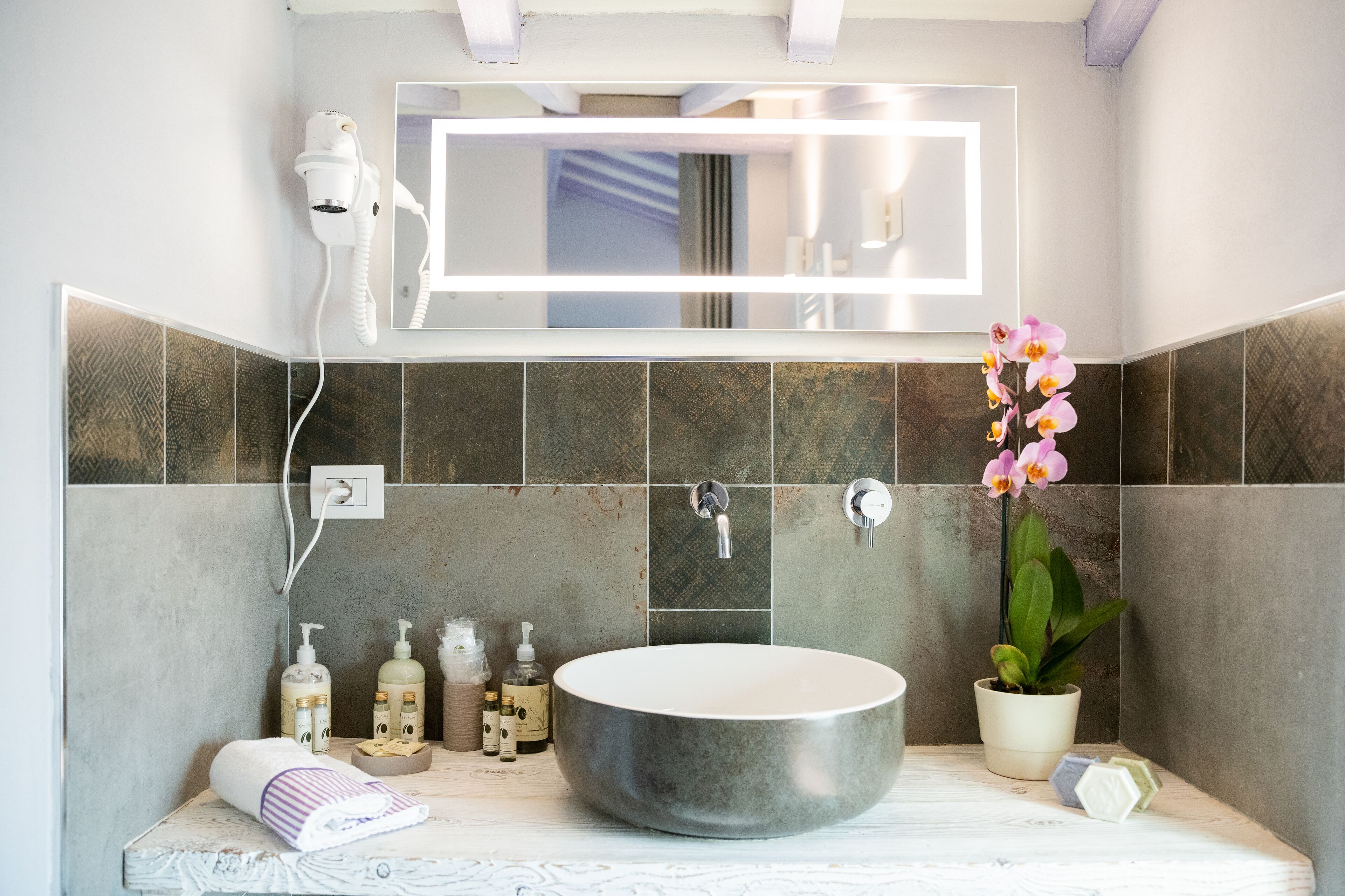 Une salle de bain moderne avec un grand lavabo rond, un sèche-cheveux fixé au mur et une orchidée en pot.