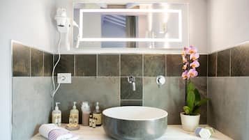 Une salle de bain moderne avec un grand lavabo rond, un sèche-cheveux fixé au mur et une orchidée en pot.