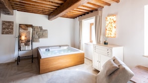 A modern bathroom with a wooden bathtub, a beige chair, and a stone wall. - Il Castelluccio Country Resort (Barberino di Mugello)