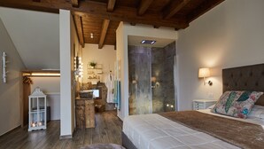 A bedroom with a large bed, a nightstand, a lamp, a wooden bench, and a bathroom with a shower and a mirror. - Il Castelluccio Country Resort (Barberino di Mugello)