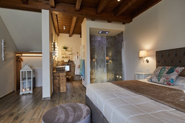 Une chambre à coucher avec un grand lit, une table de chevet, une lampe, un banc en bois et une salle de bain avec une douche et un miroir.