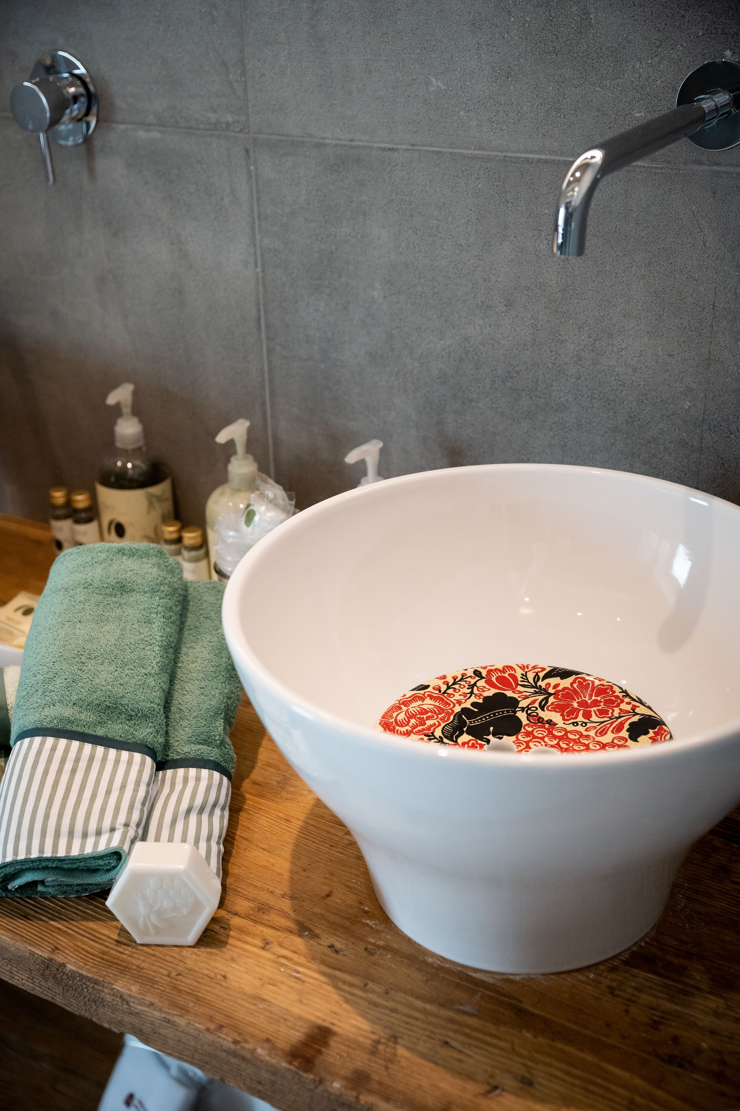 Une salle de bain avec un lavabo blanc, des serviettes vertes et des articles de toilette disposés sur un comptoir en bois.