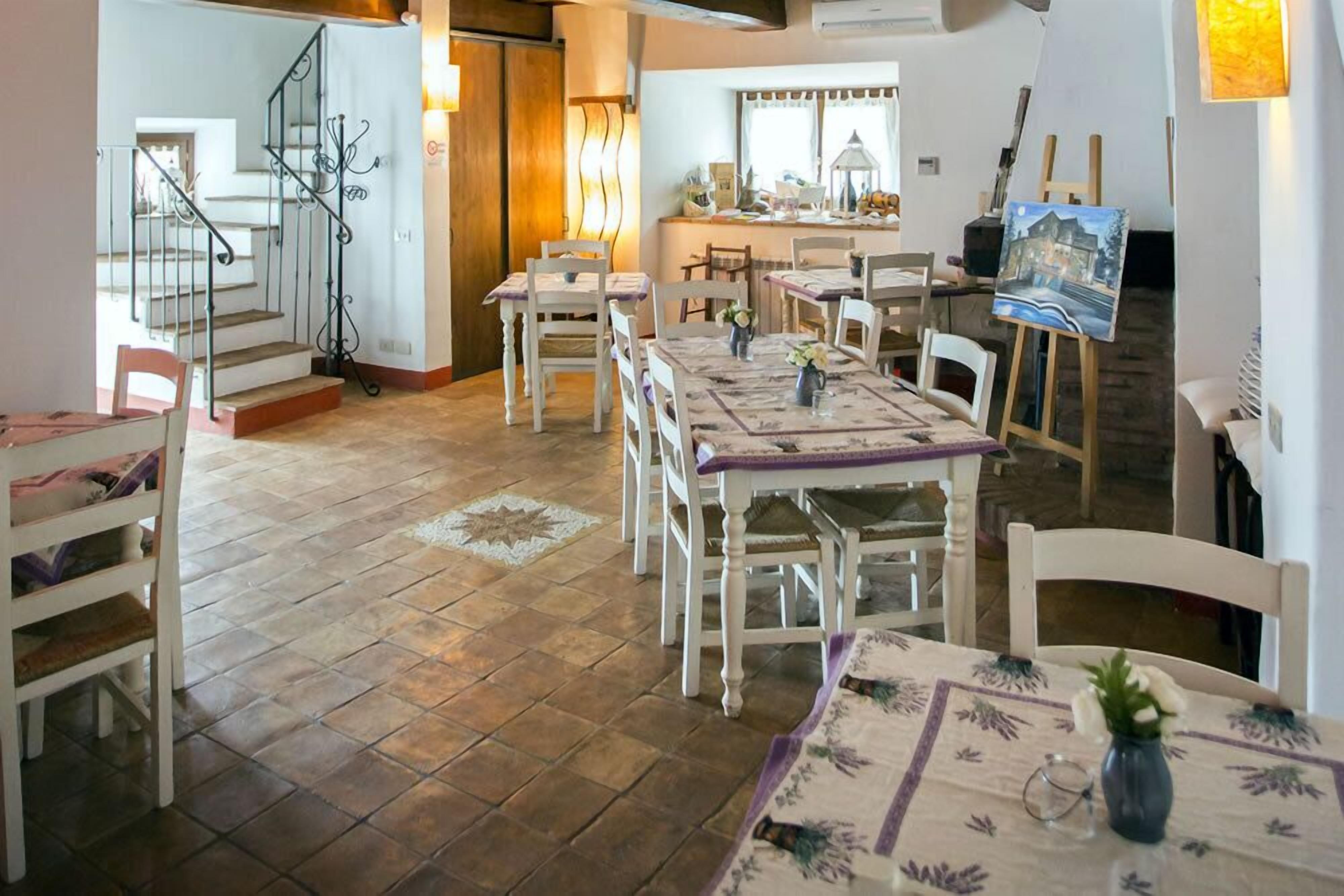 A dining area with a long table, white chairs, and a painting on easel.