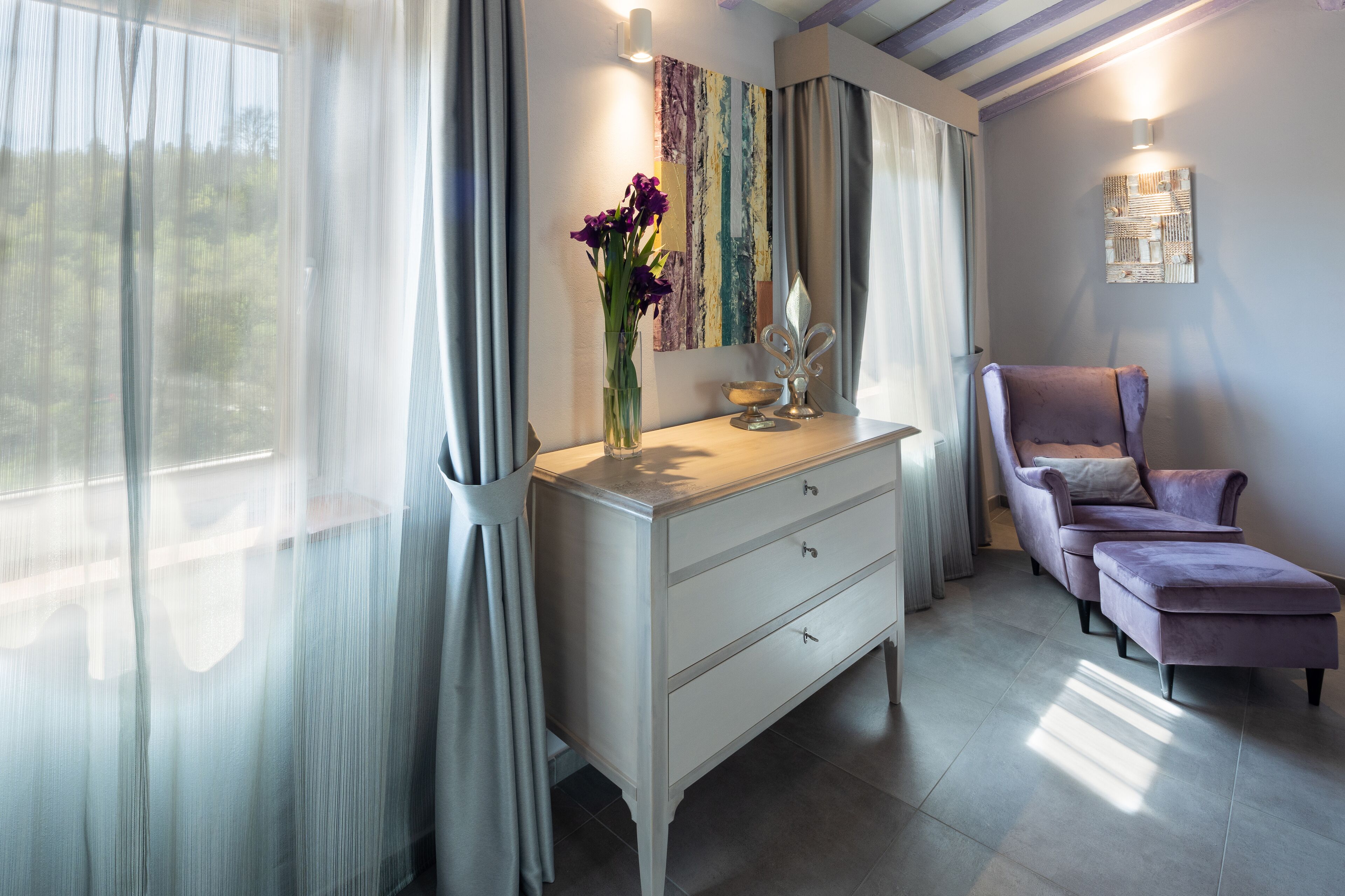 A room with a white dresser, a purple sofa, and a vase with purple flowers.