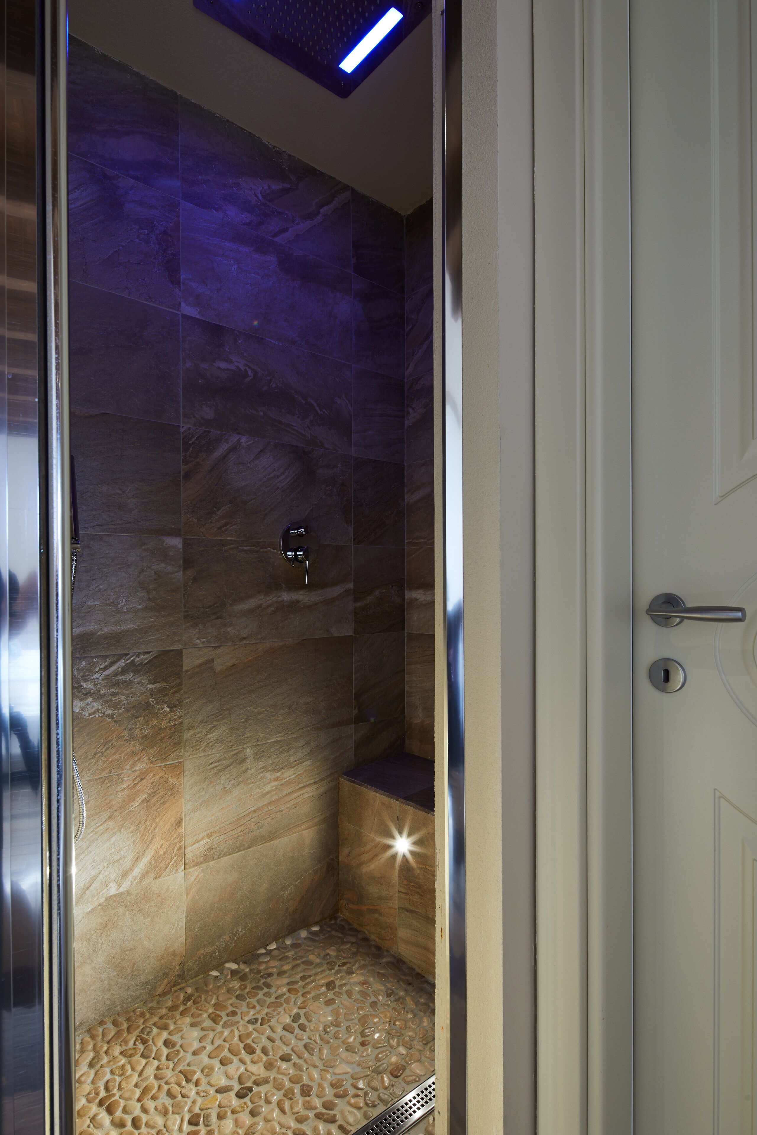 A walk-in shower with a stone floor and a blue light fixture on the ceiling.