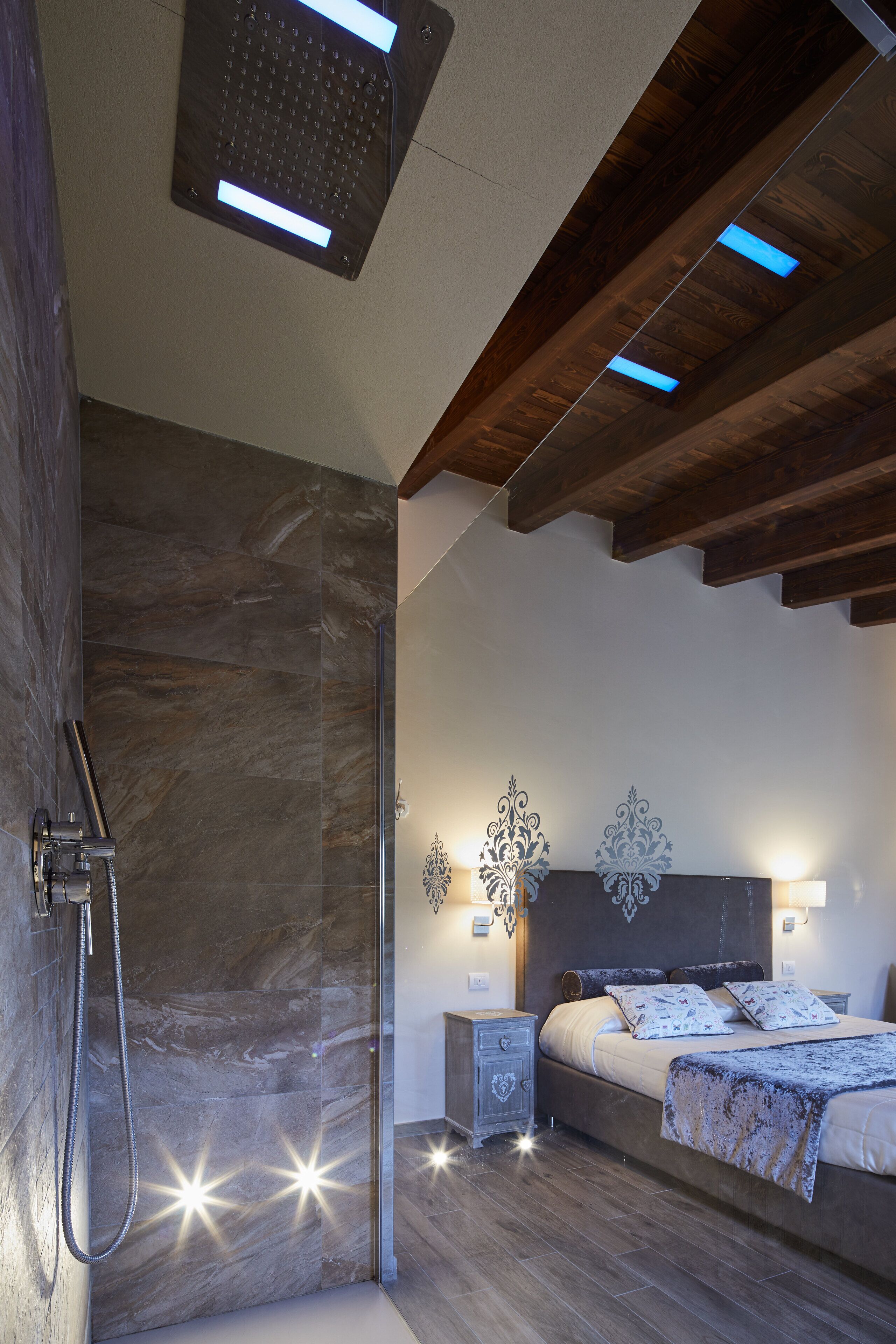 A modern bedroom with a shower, a bed with decorative pillows, and wall-mounted lights.