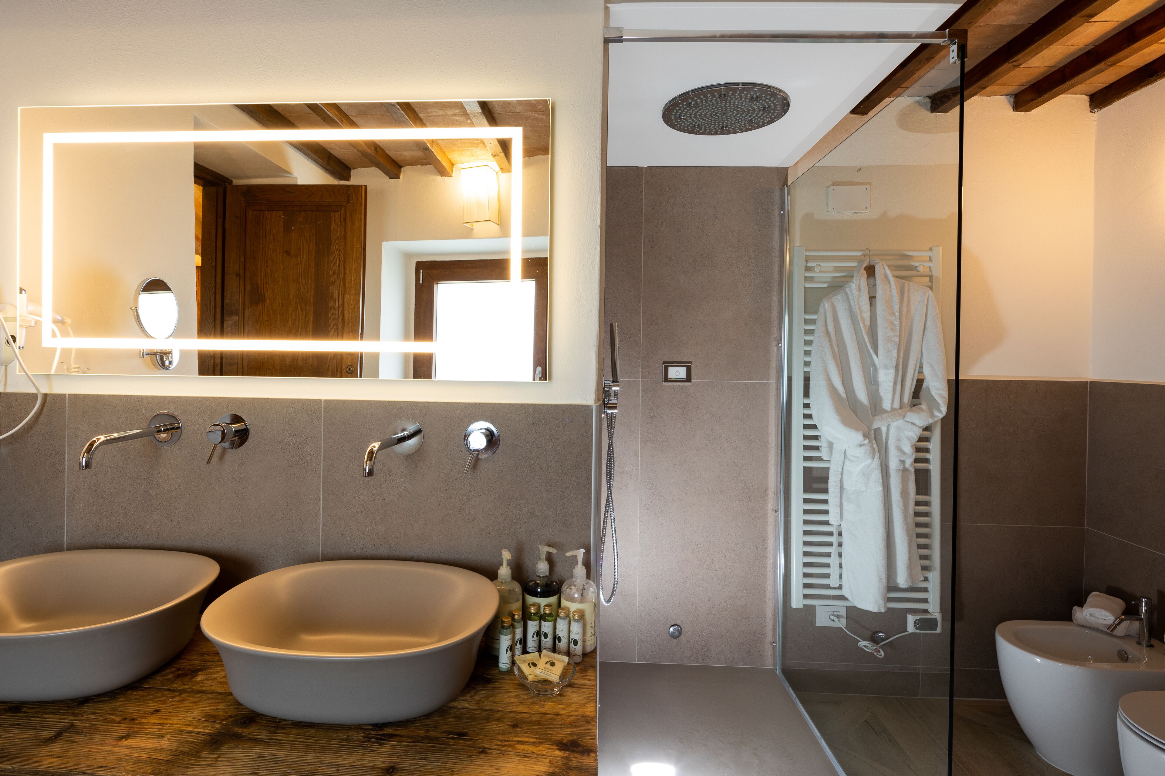 A bathroom with two sinks, a mirror with integrated lighting, a shower area, and a towel rack.