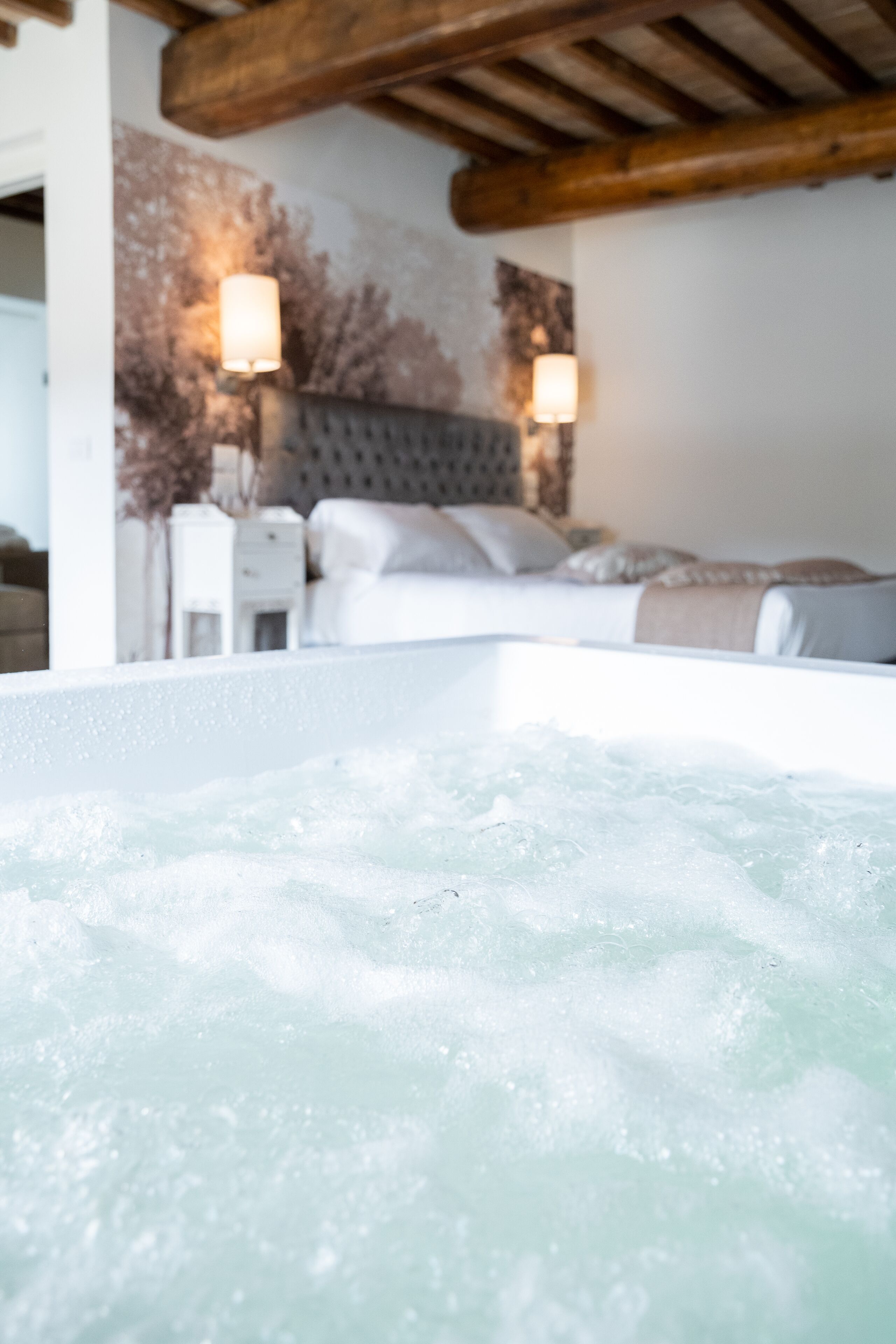 A hot tub with a wooden ceiling and a bed with a headboard in the background.