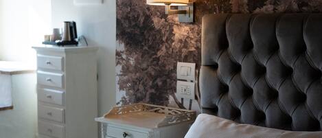 Une chambre à coucher avec une tête de lit capitonnée, une table de chevet avec une lampe, une commode et un coussin à motifs floraux.
