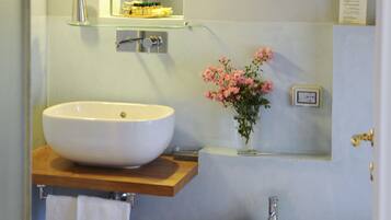 Ein Badezimmer mit einem großen weißen Waschbecken, einem Bidet, einem Spiegel und einer Vase mit Blumen.