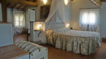 A bedroom with a bed, bedside lamps, a canopy bed, a chest of drawers, and a painting on the wall.