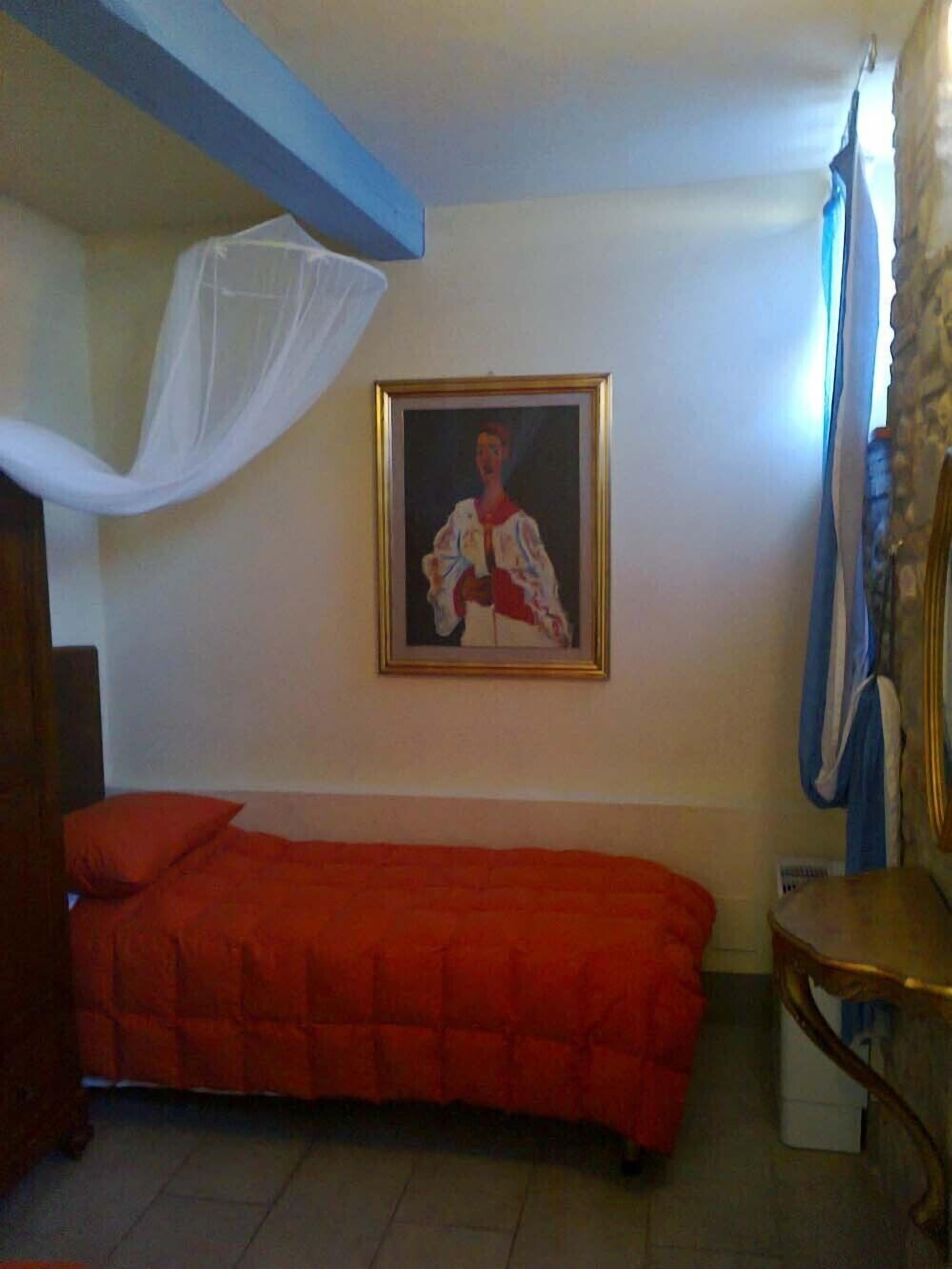 A room with a bed, a framed picture on the wall, and a chair.