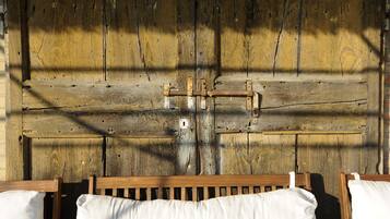 A rustic wooden wall with a metal gate, wooden benches, and white cushions.