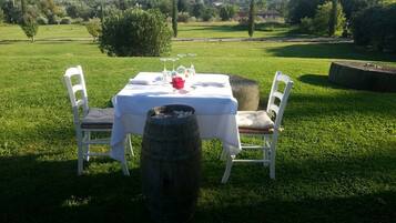 Una mesa al aire libre con mantel blanco, dos sillas blancas y un barril al frente.