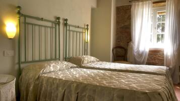 Une chambre avec deux lits, un mur en pierre et une fenêtre avec des rideaux.
