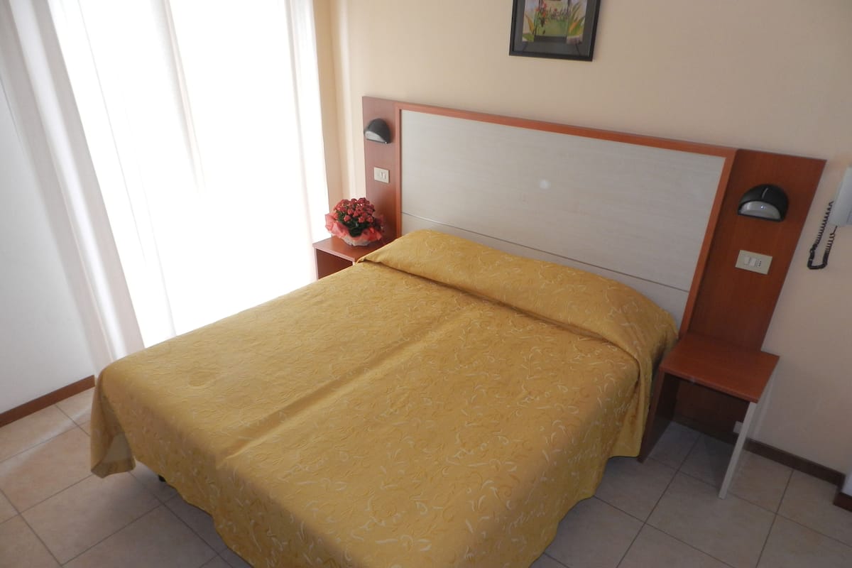 A neatly made bed with a patterned bedspread, a bedside table with a lamp, and a wall-mounted phone.