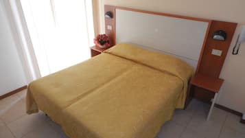 Un lit bien fait, recouvert d’une couvre-lit à motifs, une table de chevet avec une lampe et un téléphone fixé au mur.