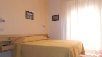 A hotel room with a bed, a nightstand, a wall-mounted lamp, and a window with curtains.