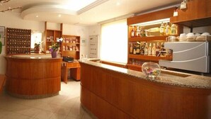A hotel lobby with a wooden reception desk, a seating area, and a bar with shelves of bottles. - Hotel Sport (Rimini)