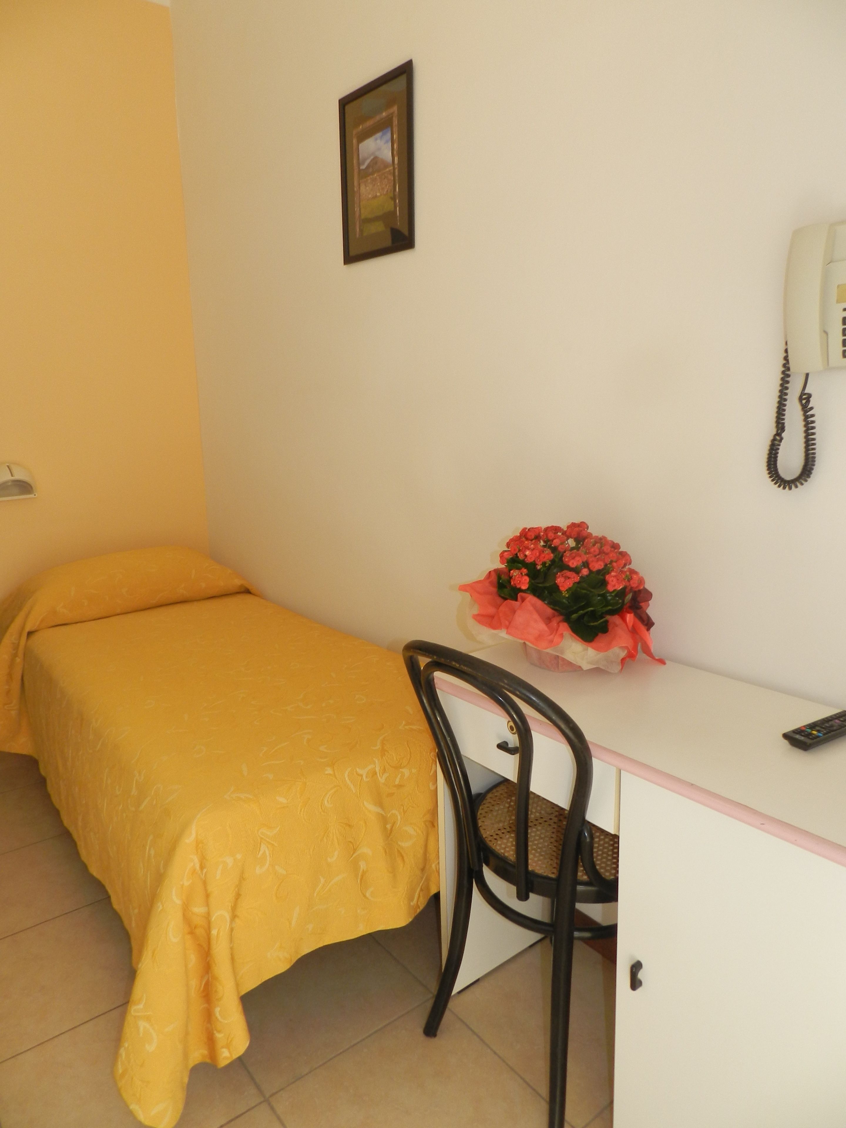 Una habitación con cama, escritorio, silla, teléfono y un ramo de flores.