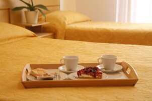Una bandeja con dos tazas y una rebanada de pastel sobre una cama con ropa de cama amarilla.
