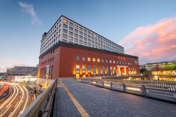 Un hotel moderno con fachada roja, varios pisos y un amplio espacio de entrada con galería techada.