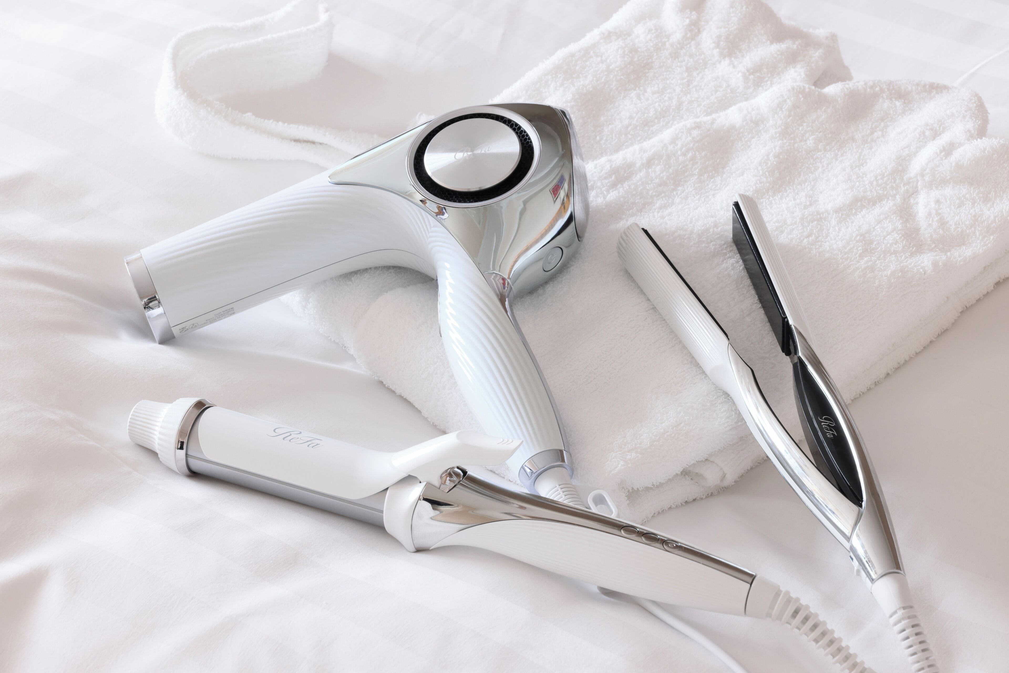 A hair dryer, scissors, and a towel on a bed.