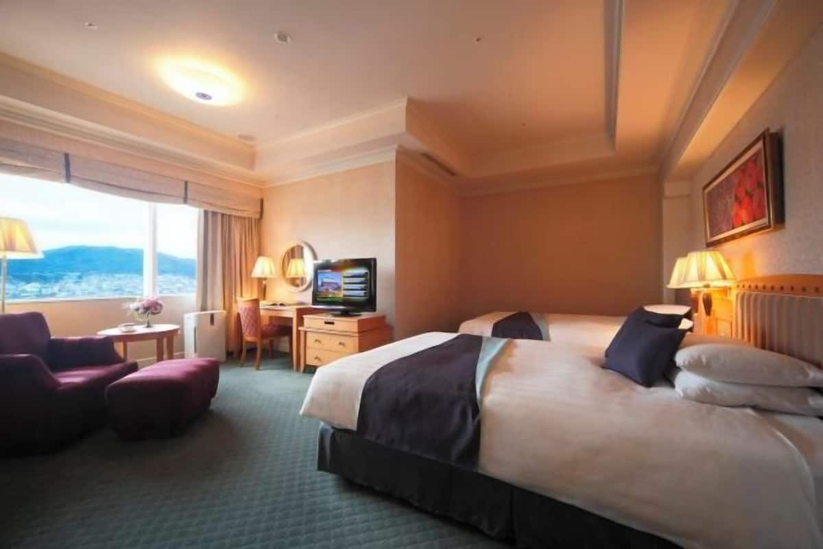 Habitación de hotel con una cama grande, un escritorio con computadora, una silla y vistas a las montañas.