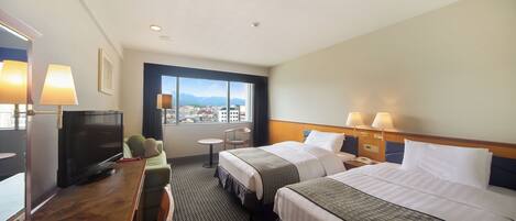 A hotel room with two beds, a desk with a TV, a chair, a small table, and a window with a city view.