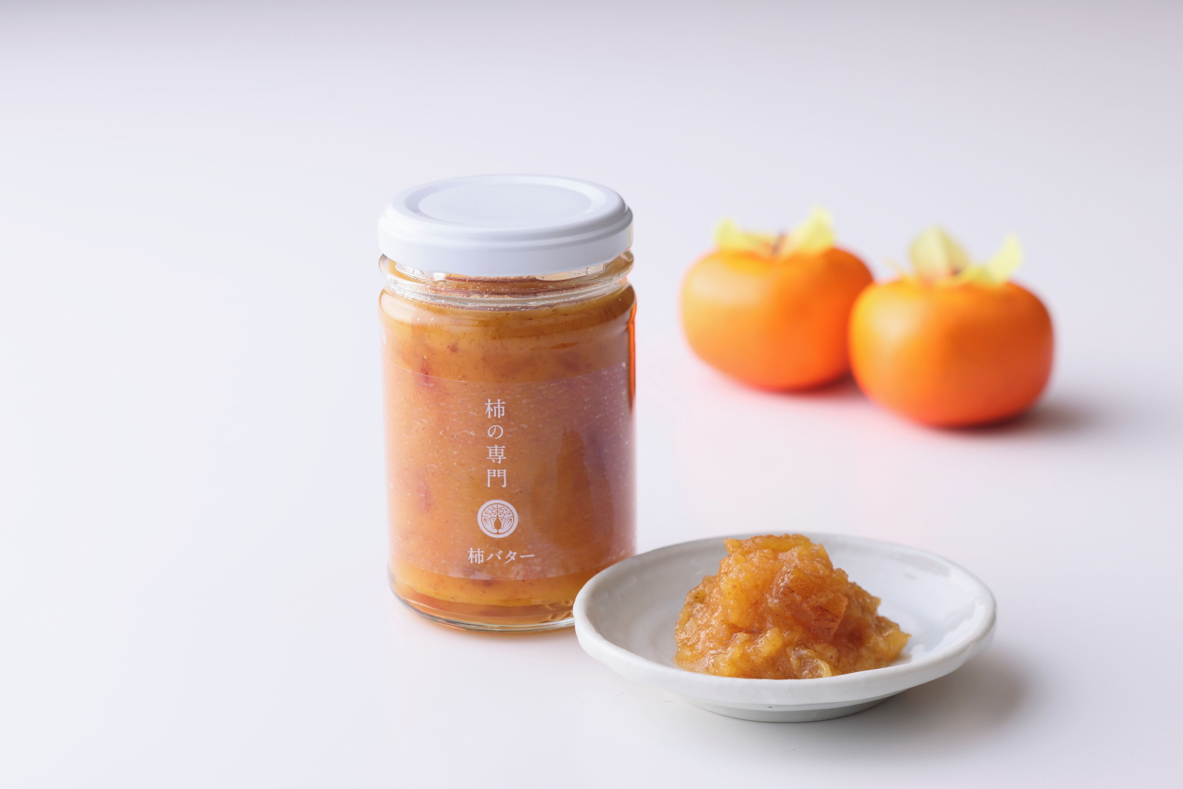 Un bocal de conserve avec un couvercle blanc, deux tomates entières et une petite assiette contenant une portion de la conserve.