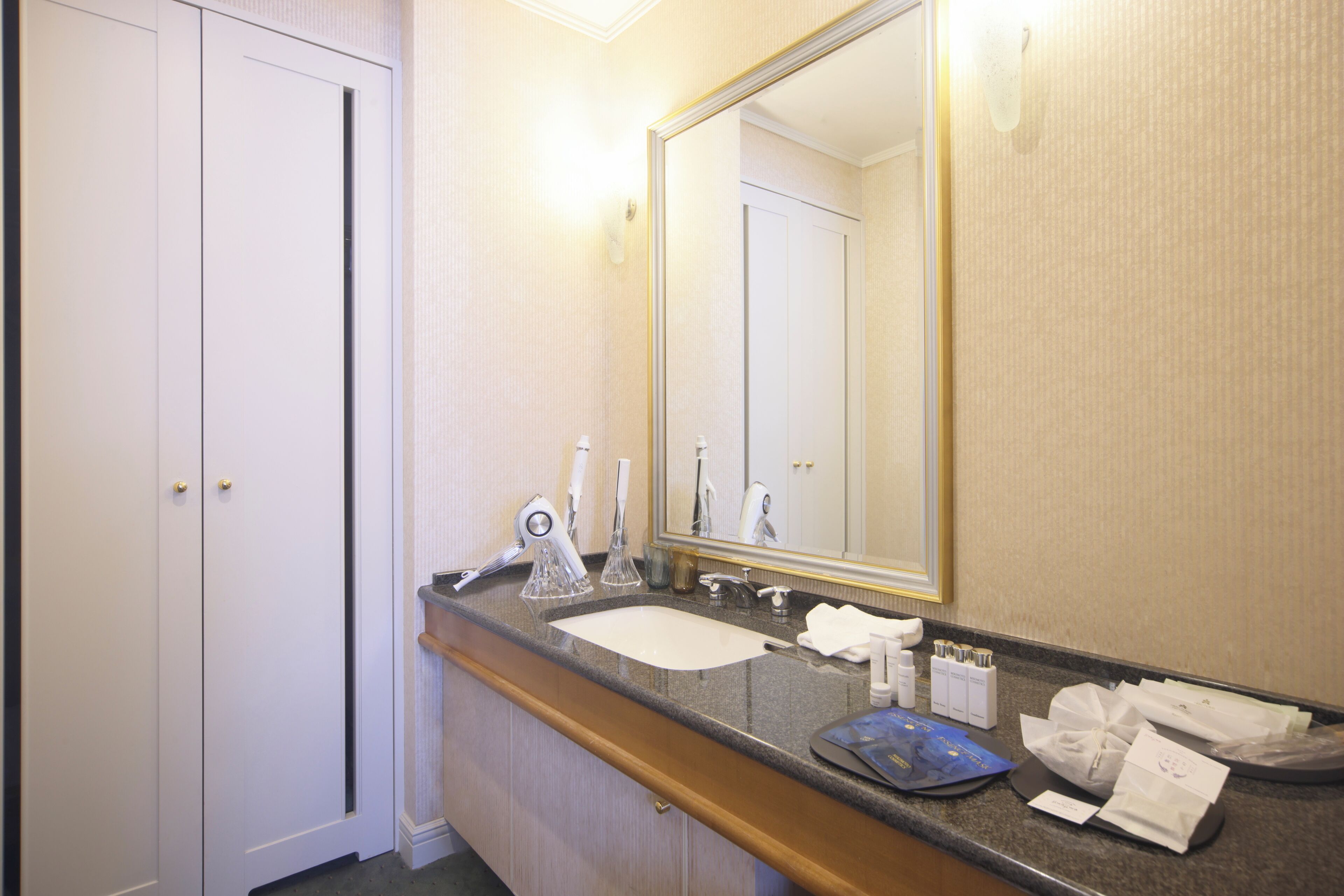 A hotel bathroom with a sink, mirror, toiletries, and a towel rack.