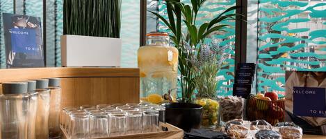 A bar area with a variety of glasses, a large pitcher, and a selection of snacks and fruits.